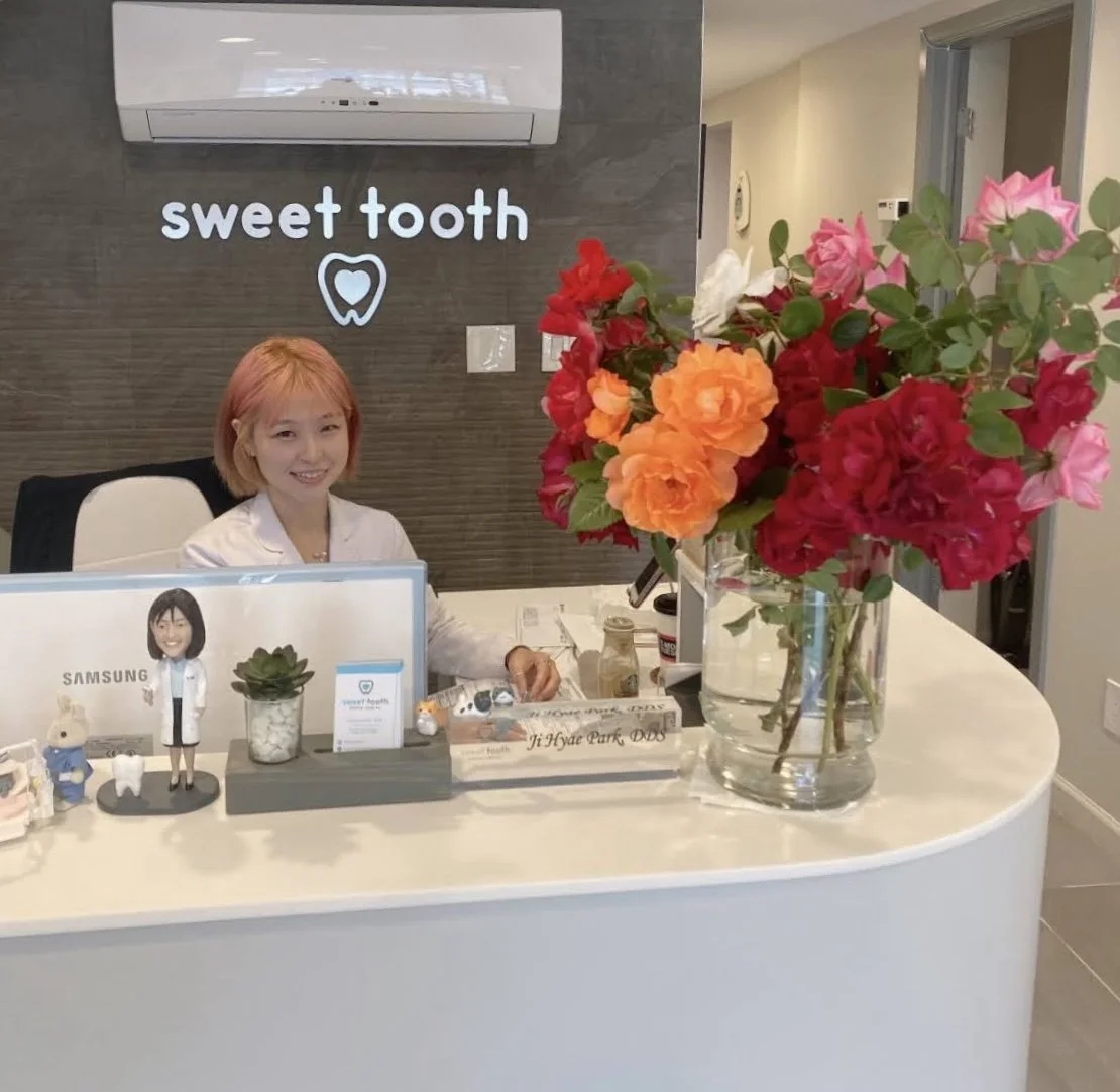 Friendly dental professional at the Sweet Tooth Dental Care front desk with bright flowers and welcoming office decor.